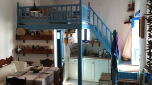 A rustic interior with a wooden staircase, a dining area with a table and chairs, and a kitchen area. - Medieval Memory House (Astypalaia)