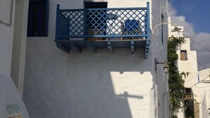 A narrow street with white buildings, a blue balcony, and a small cat on the ground. - Medieval Memory House (Astypalaia)