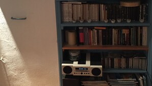 A room with a blue cabinet containing books, CDs, and a radio. - Medieval Memory House (Astypalaia)