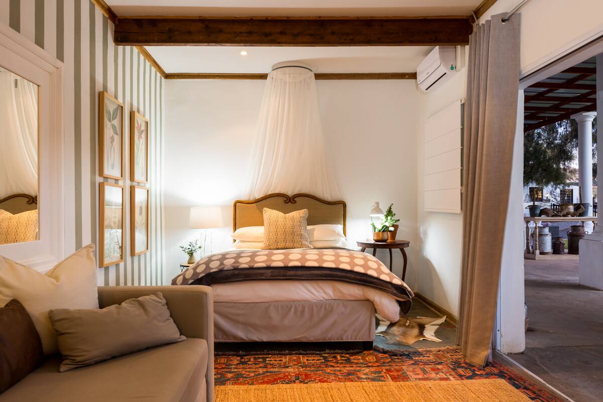Un dormitorio con cama, sofá, mesita de noche con lámpara, lámpara colgante y vistas al exterior.