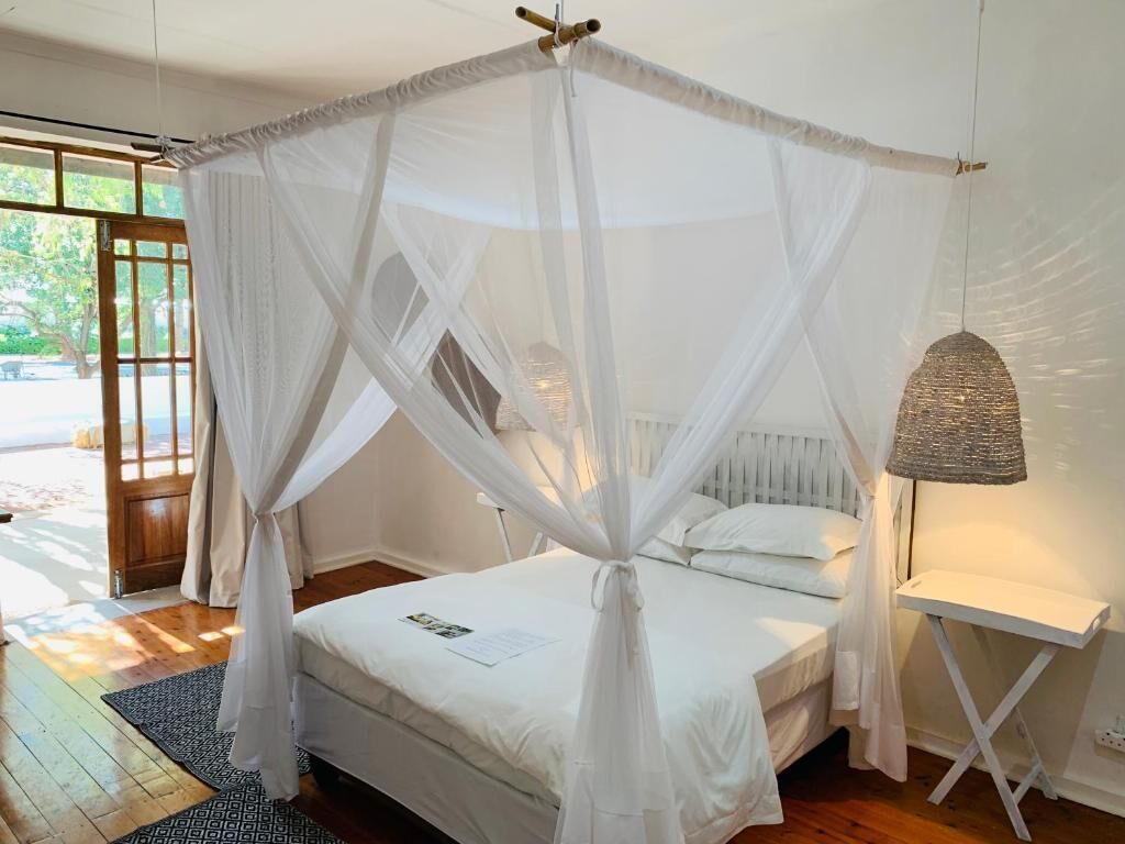 Ein Zimmer mit einem Bett unter einem weißen Baldachin, einer Nachttischlampe und Blick ins Freie.