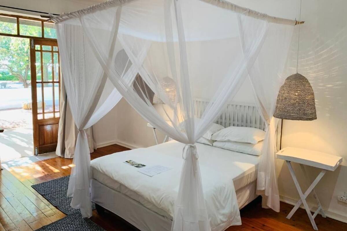 Una habitación con una cama bajo un dosel blanco, una lámpara de noche y vistas al exterior.
