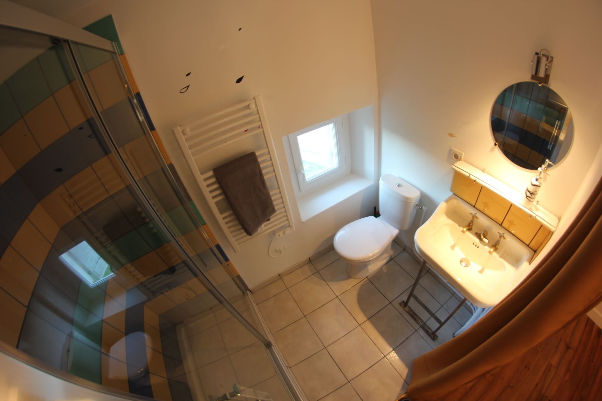 A bathroom with a toilet, sink, and mirror. There is a window providing natural light and a towel rack.