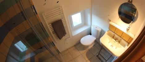 A bathroom with a toilet, sink, and mirror. There is a window providing natural light and a towel rack.