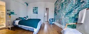 Un dormitorio con cama, mesita de noche, pared con diseño y puerta que da a otra habitación.