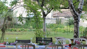 An outdoor dining area with tables set for two, surrounded by greenery and trees.