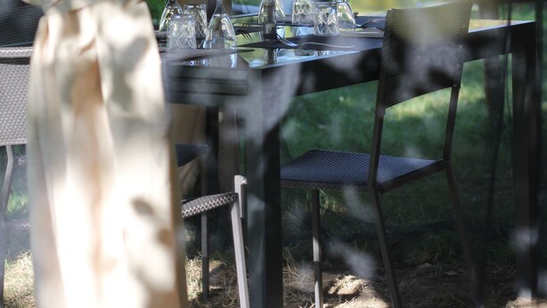 A dining table set outdoors with chairs, a tablecloth, and several wine glasses.