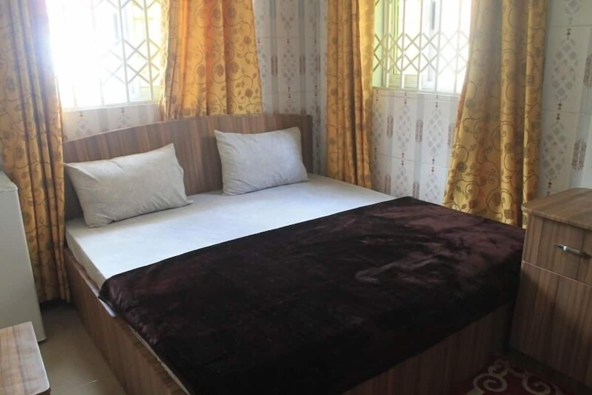 A single bed with a dark-colored blanket, two pillows, and a wooden headboard.
