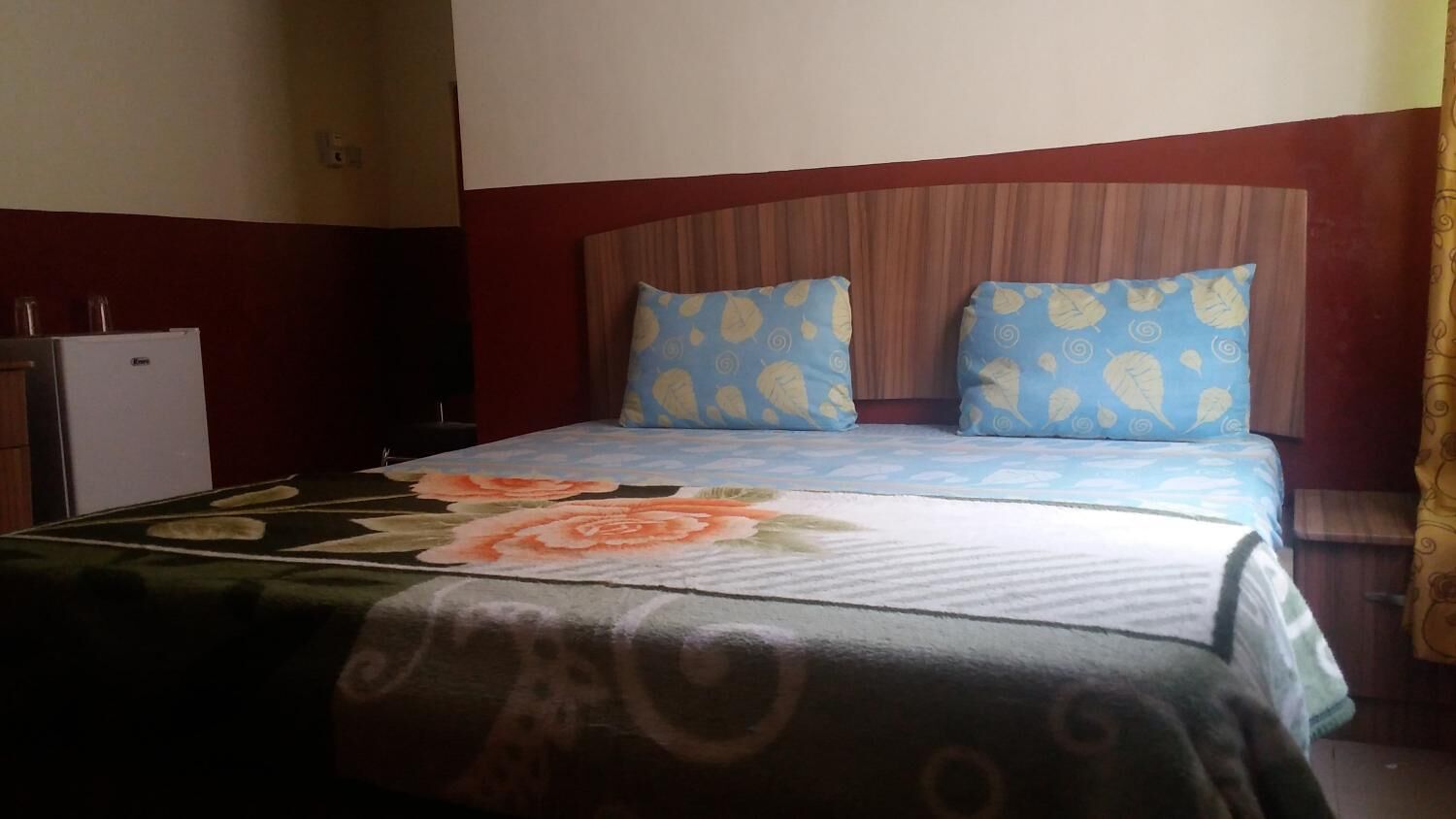 Habitación de hotel con cama, dos almohadas, mesita de noche y refrigerador.