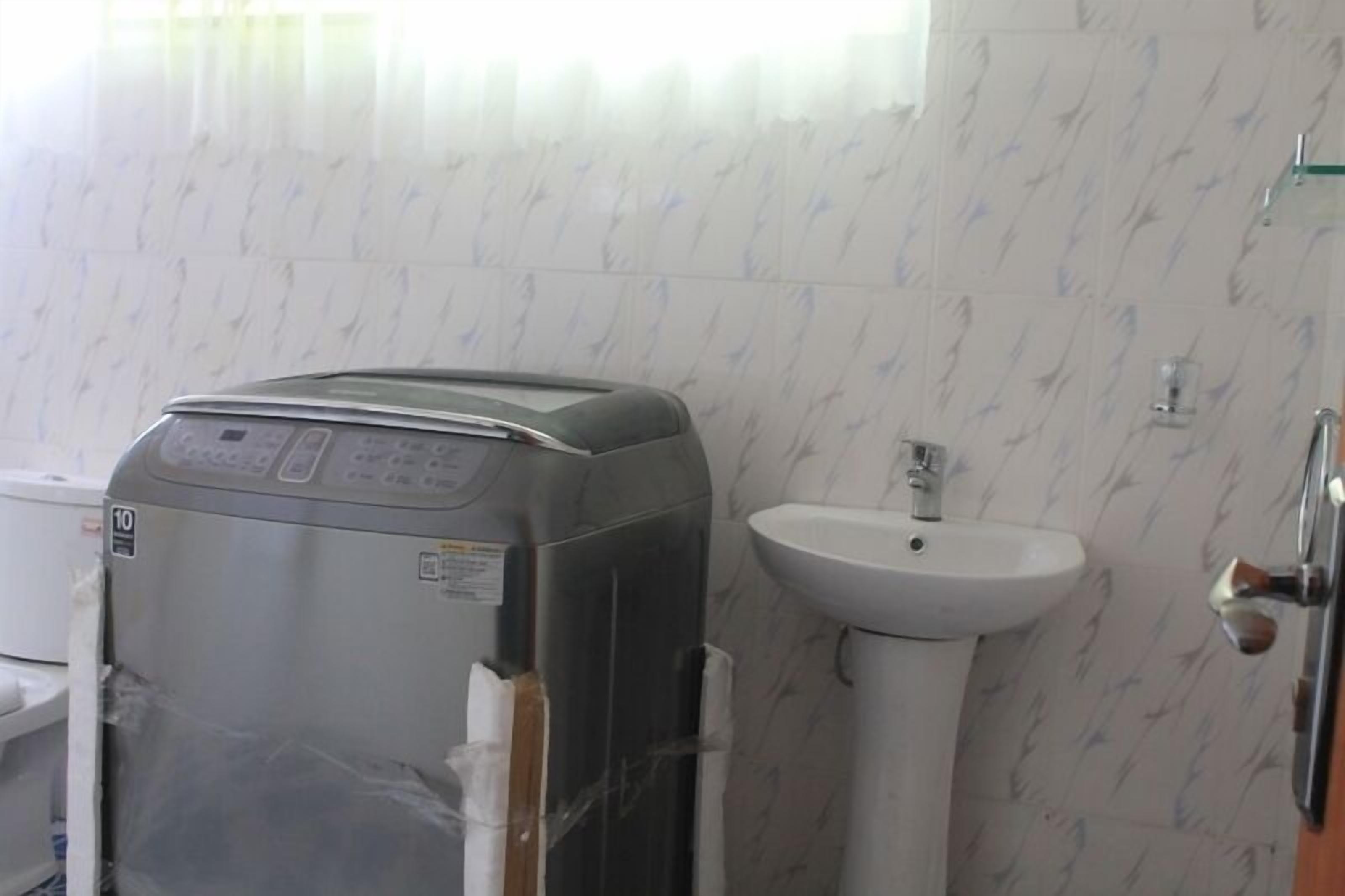 Ein kleines Badezimmer mit einem grauen Warmwasserbereiter, einem weißen Waschbecken und Wandfliesen mit Muster.