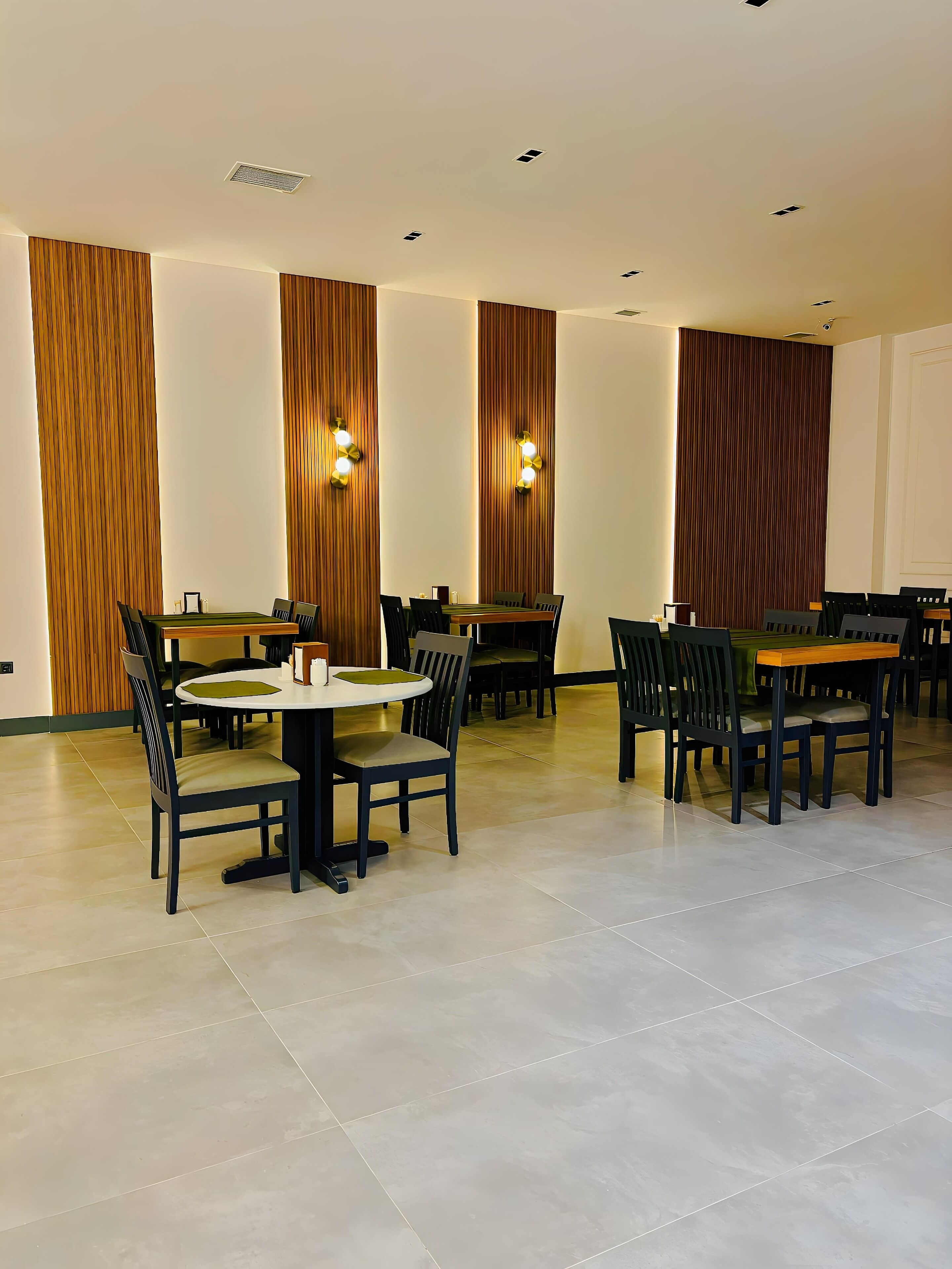 A spacious dining area with multiple tables and chairs, wooden paneling on the walls, and recessed ceiling lighting.