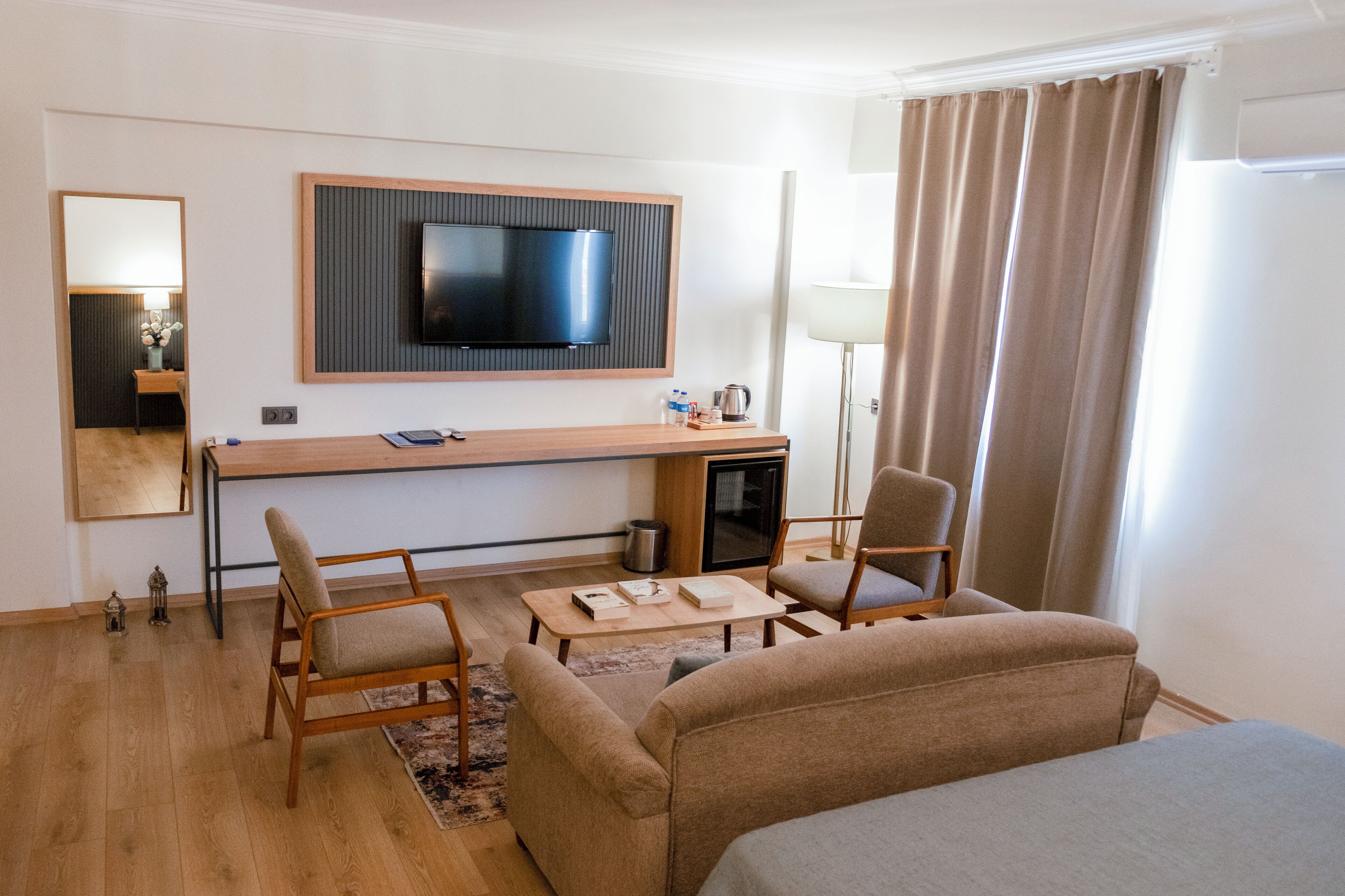 A hotel room with a bed, a desk with a TV, two chairs, a lamp, and a small table.