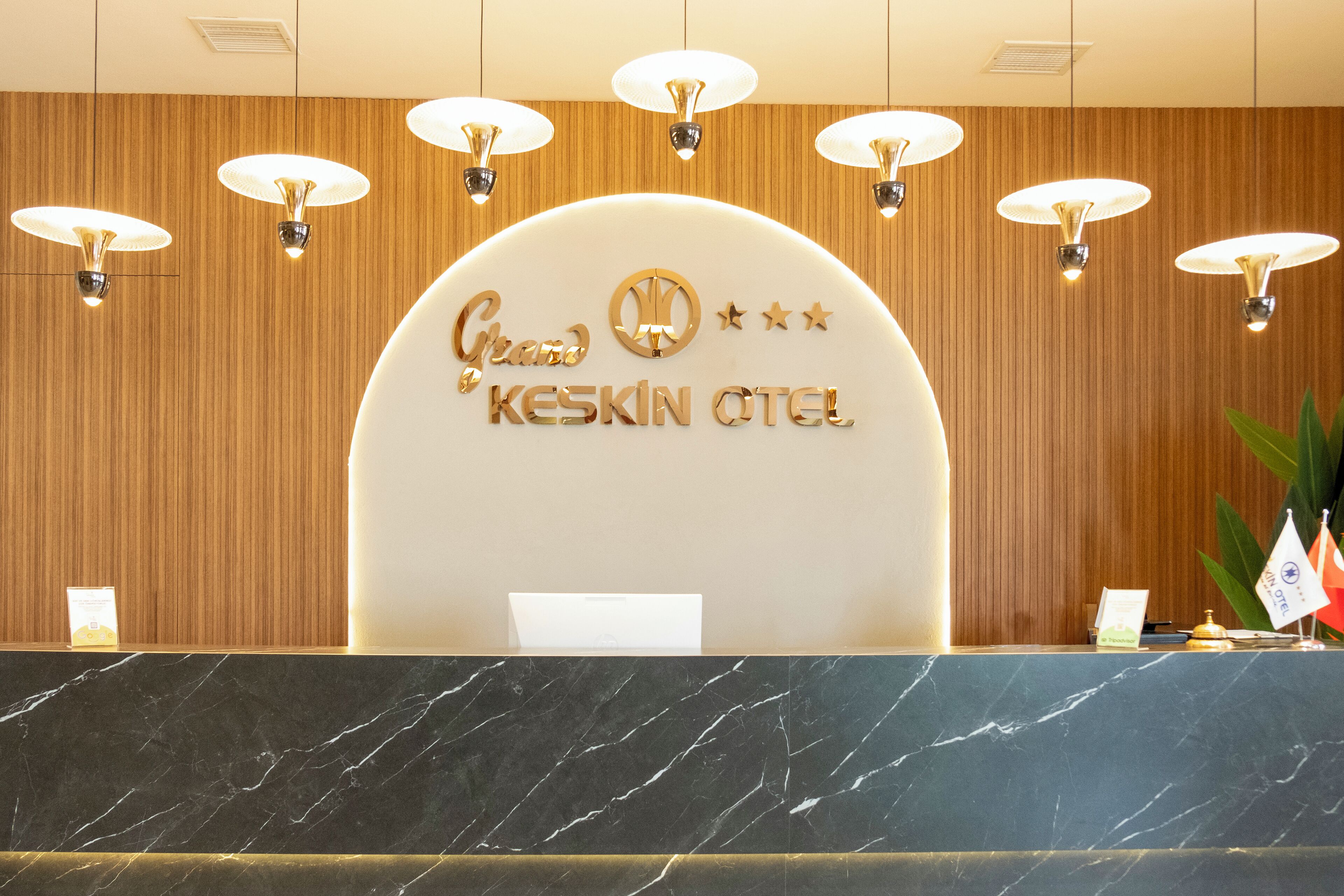 Un comptoir d’accueil d’hôtel avec un comptoir en marbre, un mur en bois et une enseigne sur laquelle on peut lire « Grand KESKIN OTEL ».