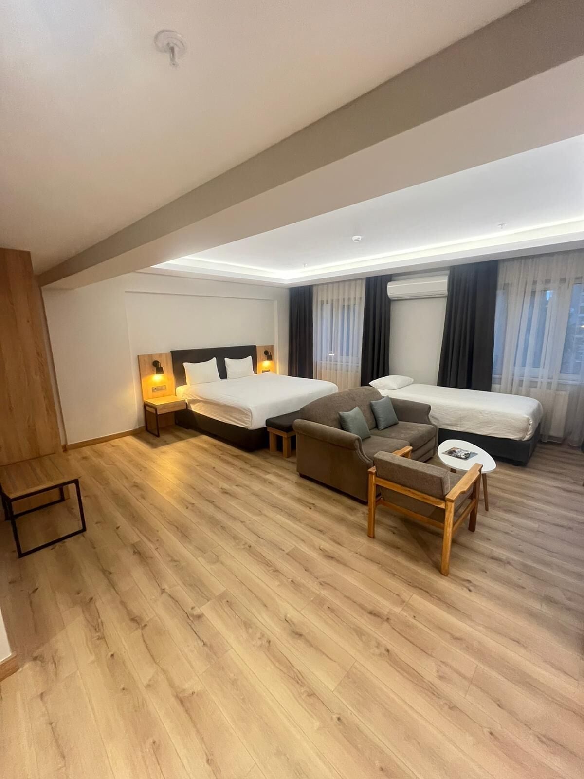 Una habitación de hotel moderna con dos camas, un sofá, una mesita y suelo de madera.