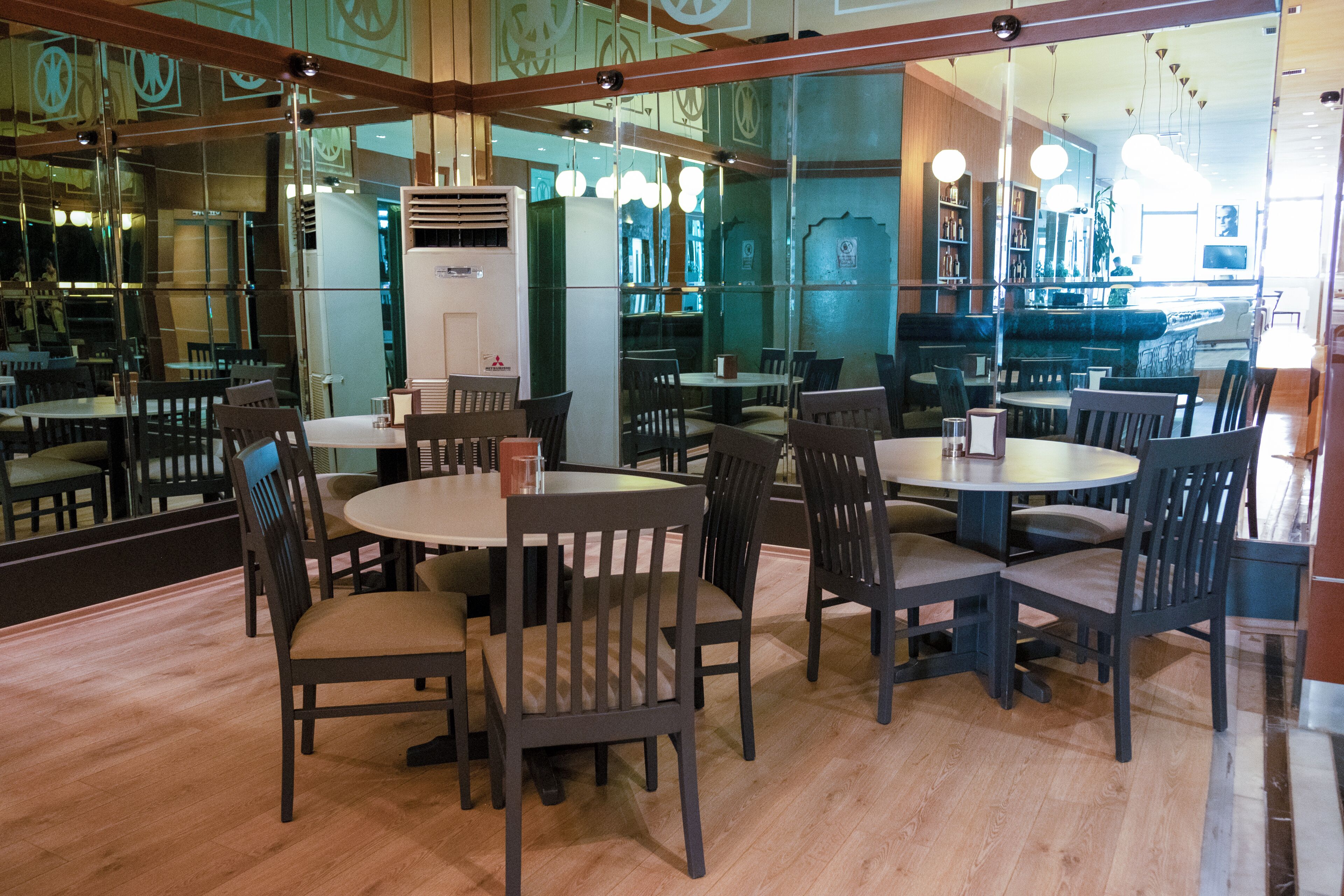 A restaurant with round tables and chairs, a large mirror, and a view of the bar area.