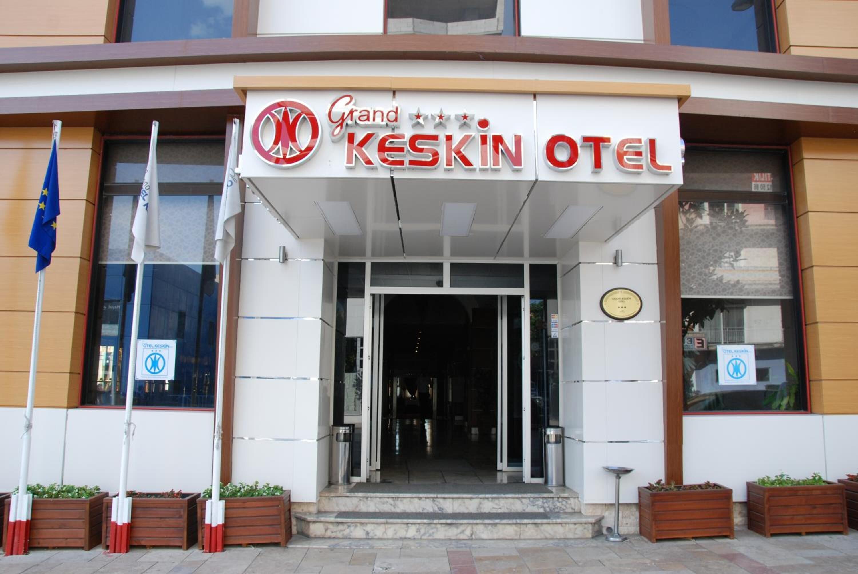 La entrada del Hotel Grand Keskin, con un letrero visible, una bandera y un cartel de prohibido estacionar.