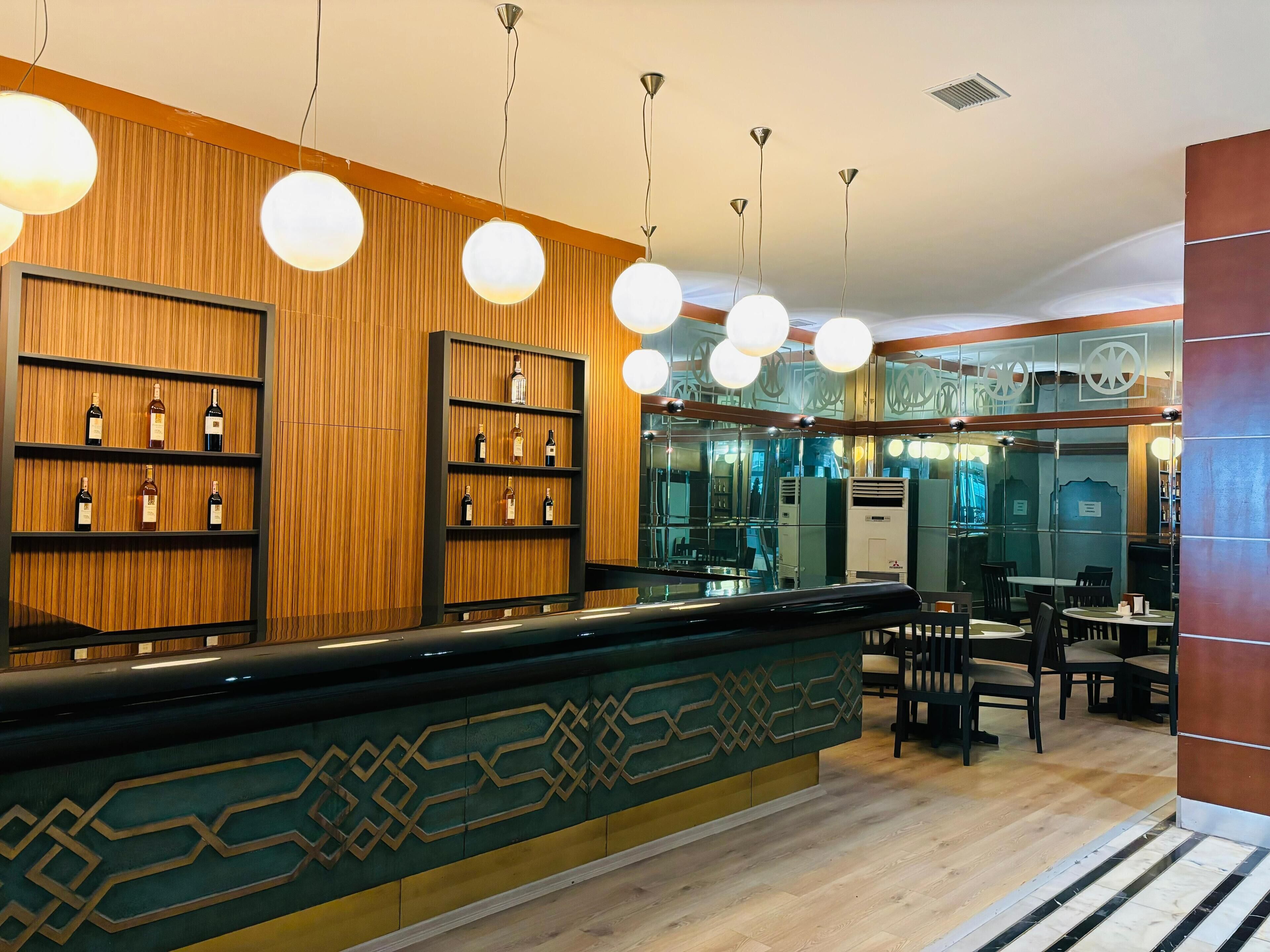 A hotel lobby with wooden paneling, a reception desk with a patterned design, and multiple wine bottles displayed on shelves.