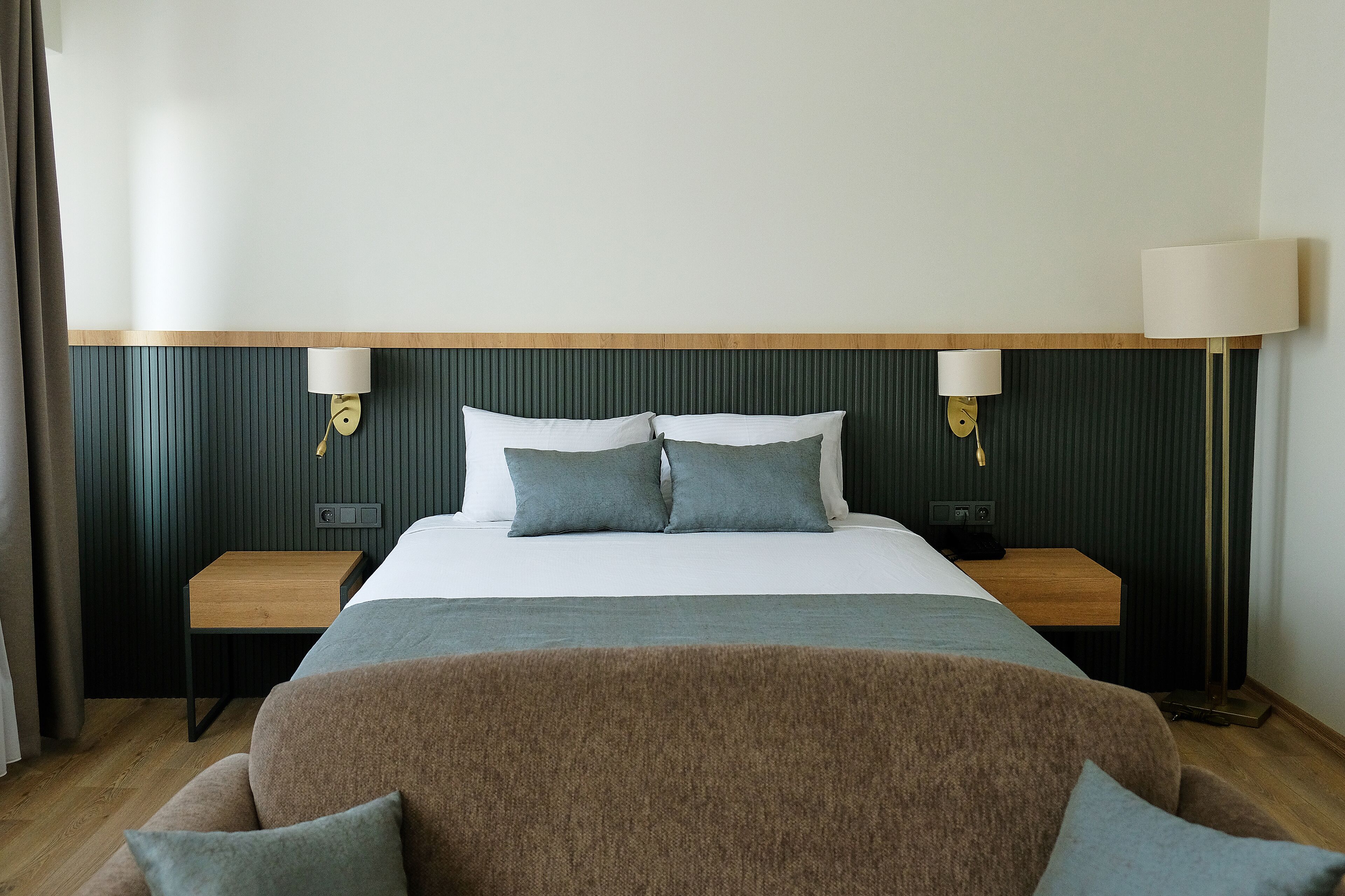 Habitación de hotel con una cama, dos mesitas de noche, un escritorio de madera y un sofá.