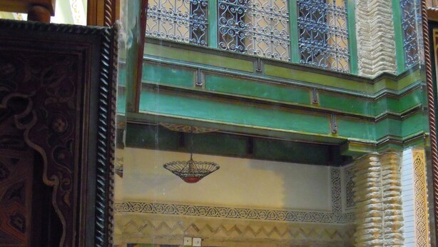 A traditional Moroccan interior with ornate wooden doors, a decorative archway, and a green metal balcony railing. - Museum House - Dar Melyani (Fes)