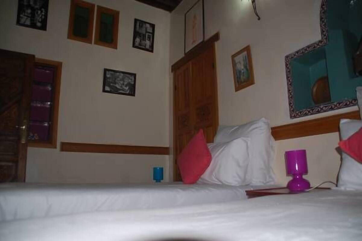 A hotel room with a bed, a wooden headboard, a mirror, and framed pictures on the wall.