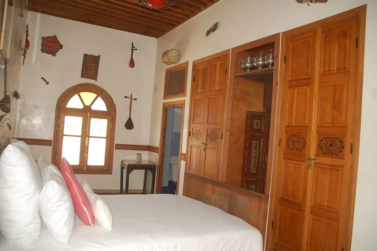 A bedroom with a large bed, wooden wardrobe, and a small table.