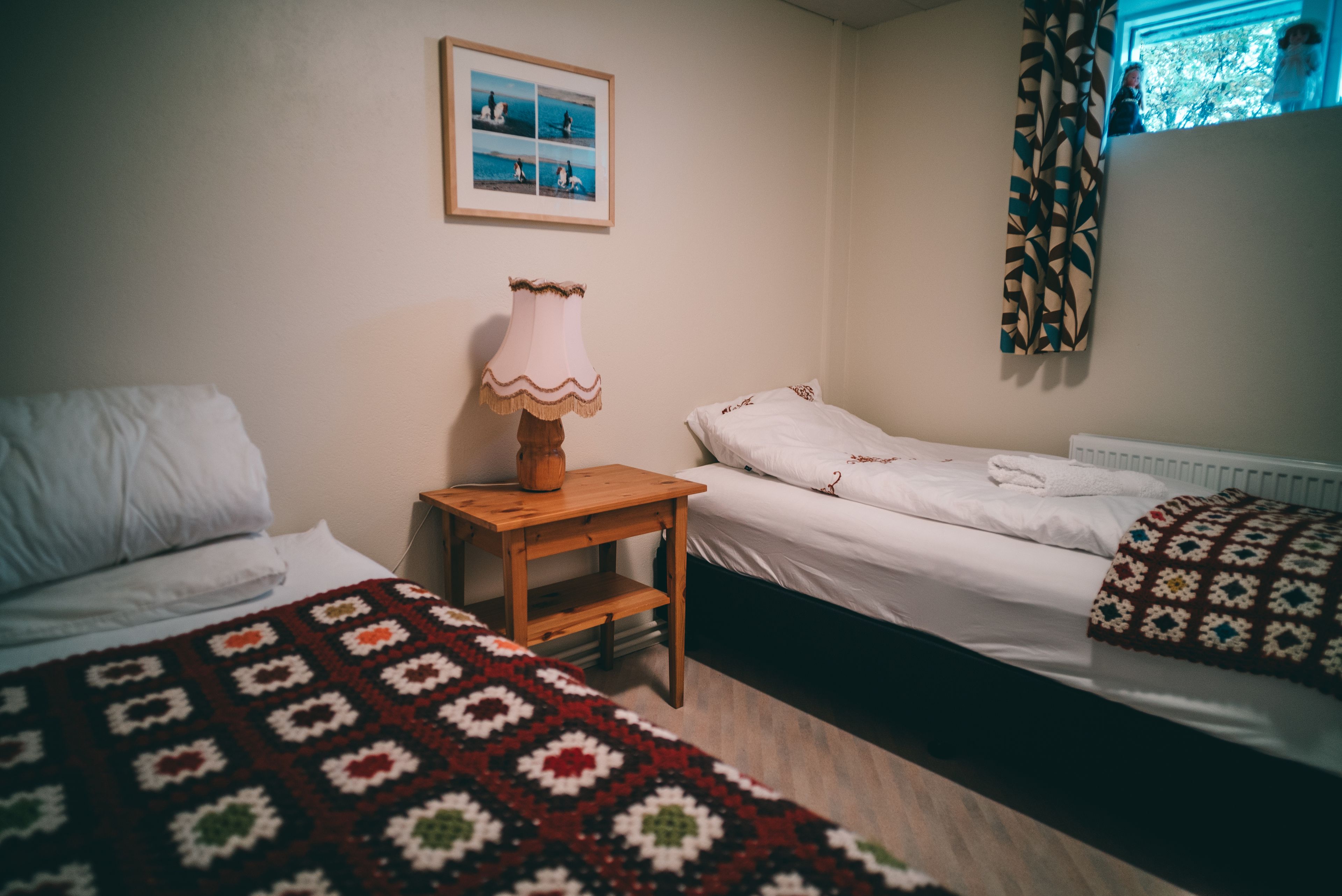 Een kamer met twee bedden, een houten nachtkastje, een lamp en een lijst met een foto aan de muur.