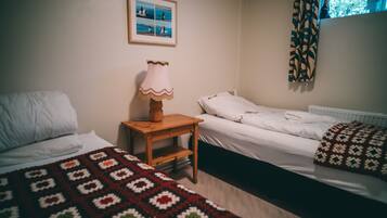 Een kamer met twee bedden, een houten nachtkastje, een lamp en een lijst met een foto aan de muur.