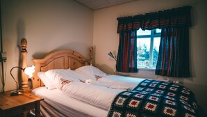 A neatly made bed with a patterned blanket, a wooden headboard, and a bedside lamp. - Bessastadir Guesthouse (Hvammstangi)