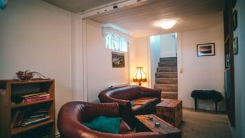 Ein gemütliches Wohnzimmer mit Ledersofas, einem Holztisch und einem Bücherregal. Eine Treppe führt in einen anderen Raum.