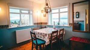 A dining area with a table set for four, wooden chairs, a radiator, and a view of the outdoors through large windows. - Bessastadir Guesthouse (Hvammstangi)