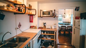 A compact kitchen with a sink, microwave, and wooden shelves. - Bessastadir Guesthouse (Hvammstangi)