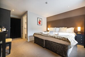 Quarto de hotel com cama grande, luminárias de cabeceira, uma mesa de trabalho e um guarda-roupa.