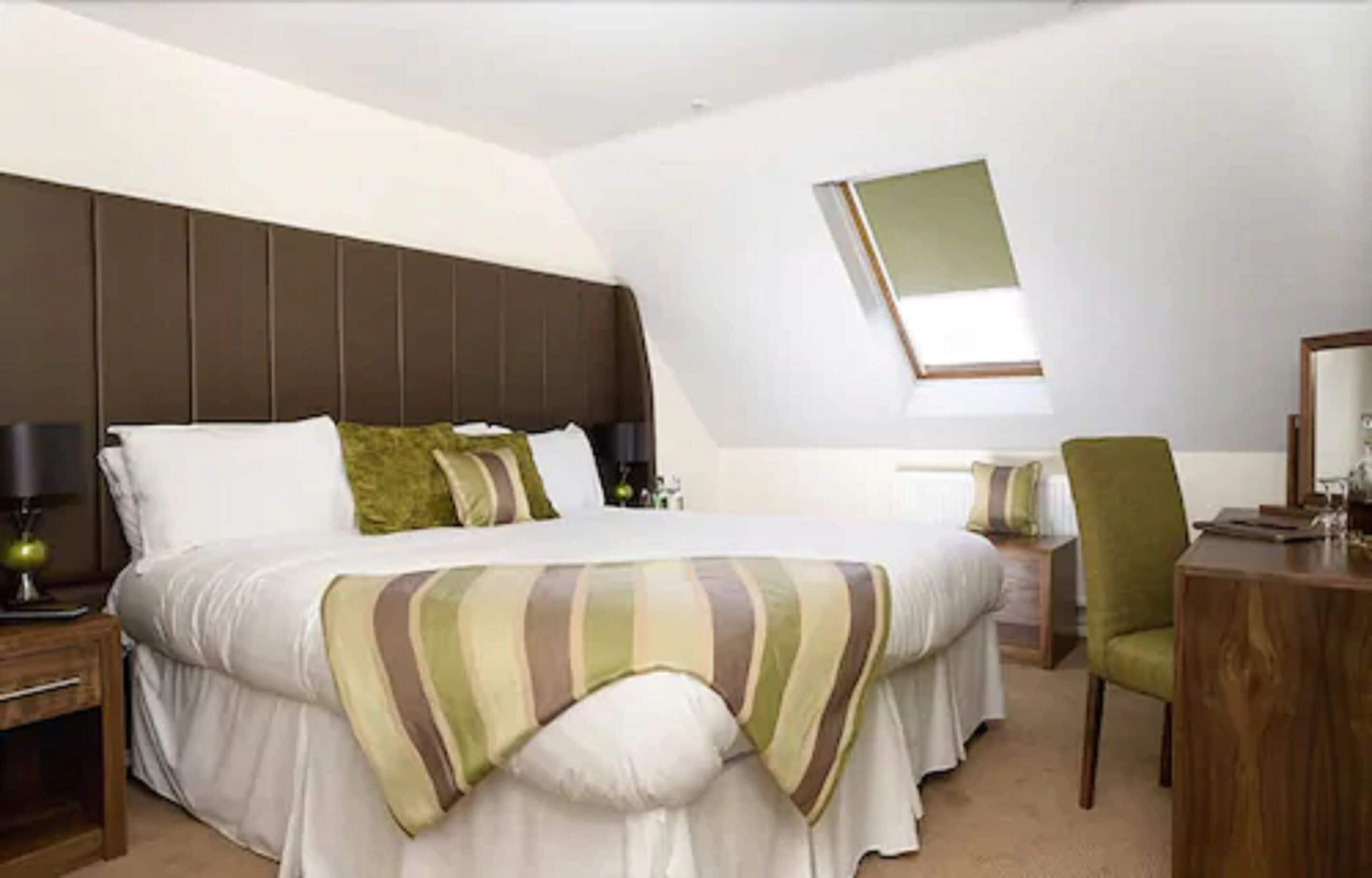 A hotel room with a large bed, a desk, a chair, and a mirror on the wall.