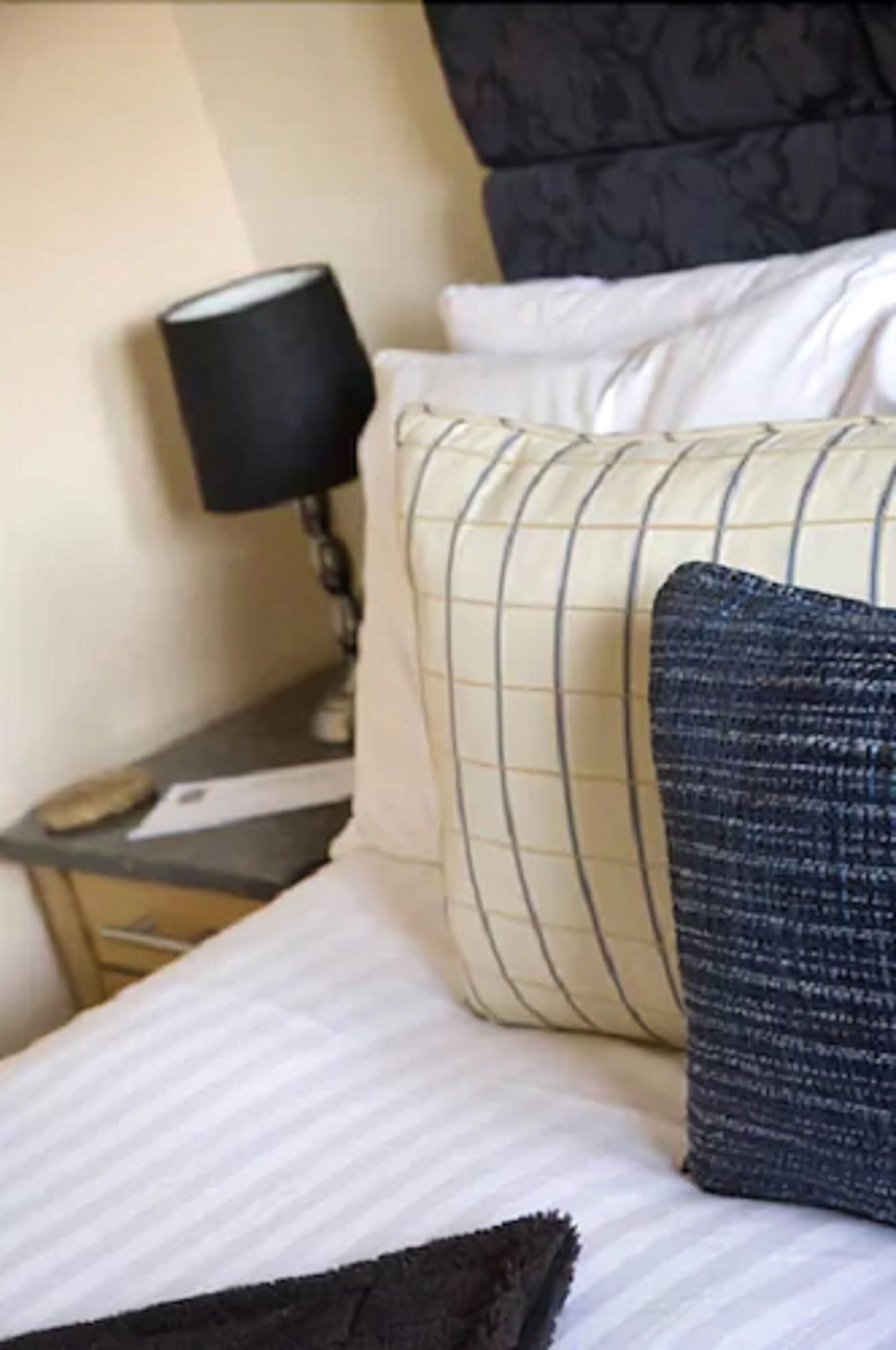 A hotel room with a bed, pillows, a nightstand, and a lamp.