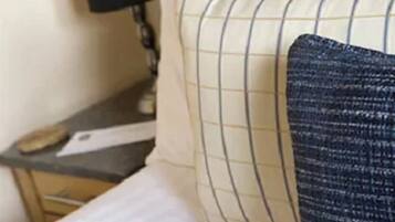 A hotel room with a bed, pillows, a nightstand, and a lamp.