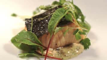Un plat composé d’un morceau de poisson, de légumes verts et d’une sauce, le tout servi dans une assiette blanche.