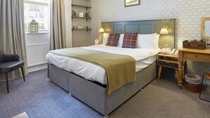 Een verzorgde hotelkamer met een bed, nachtkastje, lamp en een stoel.