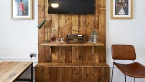 Een kamer met een houten wandpaneel, een wandgemonteerde flatscreen-tv, een houten bank en een bruine stoel.