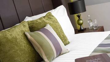 A neatly made bed with green and striped pillows, a bedside lamp, and a book titled "Rosedale Arms."