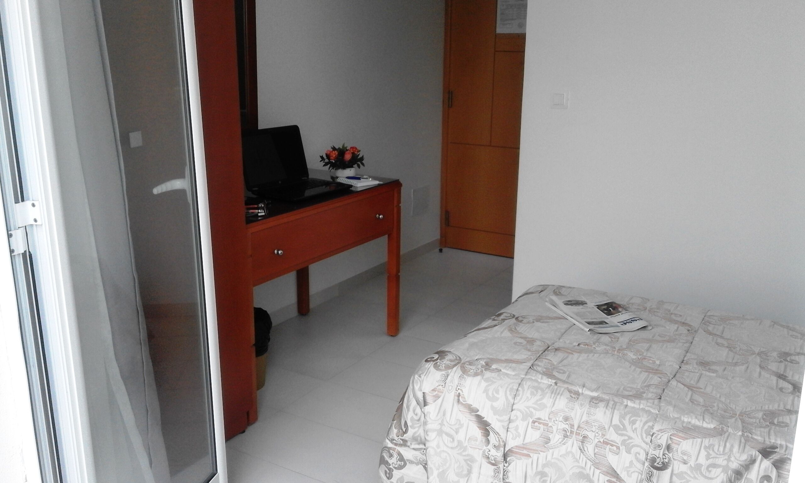 A bedroom with a bed, a desk with a laptop, a small table with a plant, and a wardrobe.