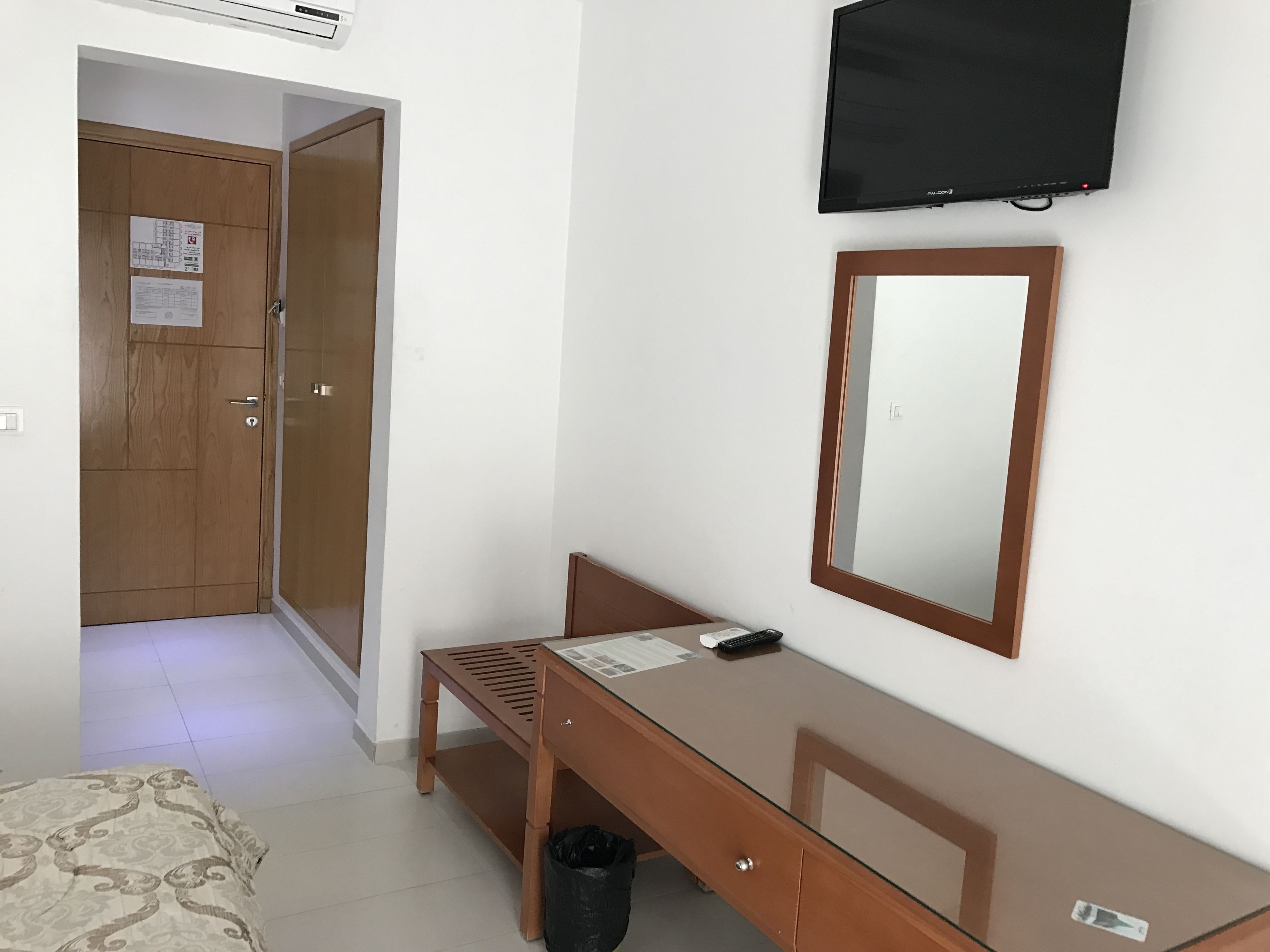 Ein Hotelzimmer mit Holzschrank, Glastisch, Spiegel, Fernseher und einem Bett mit Musterdecke.
