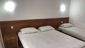 A hotel room with two single beds, a wooden headboard, a nightstand, and a small drawer.