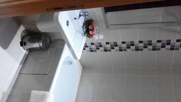 Un baño con lavamanos blanco, un espejo y piso de baldosas.
