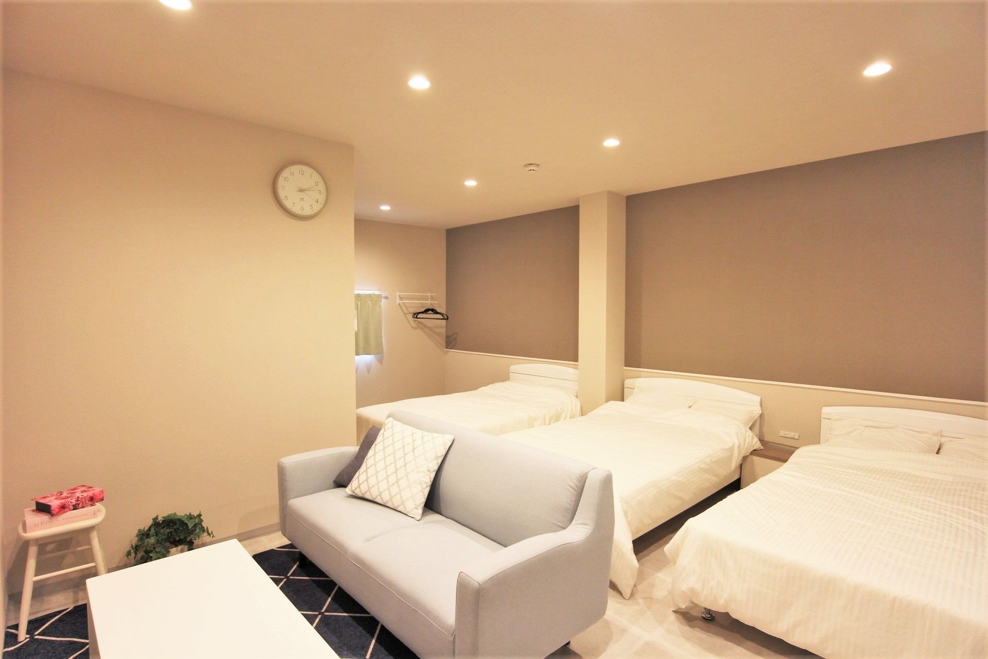 Ein Hotelzimmer mit zwei Betten, einem Sofa, einem kleinen Tisch und einer Wanduhr.