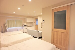 Una habitación de hotel con dos camas, una kitchenette y una puerta corredera.