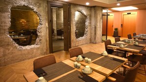 Un salón de conferencias con mesas de madera, sillas y una pared de piedra con un gran agujero.