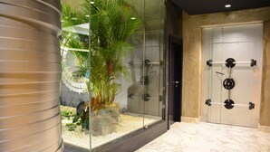 Un moderno vestíbulo de hotel con un recinto de vidrio que contiene una planta de palma y rocas decorativas.
