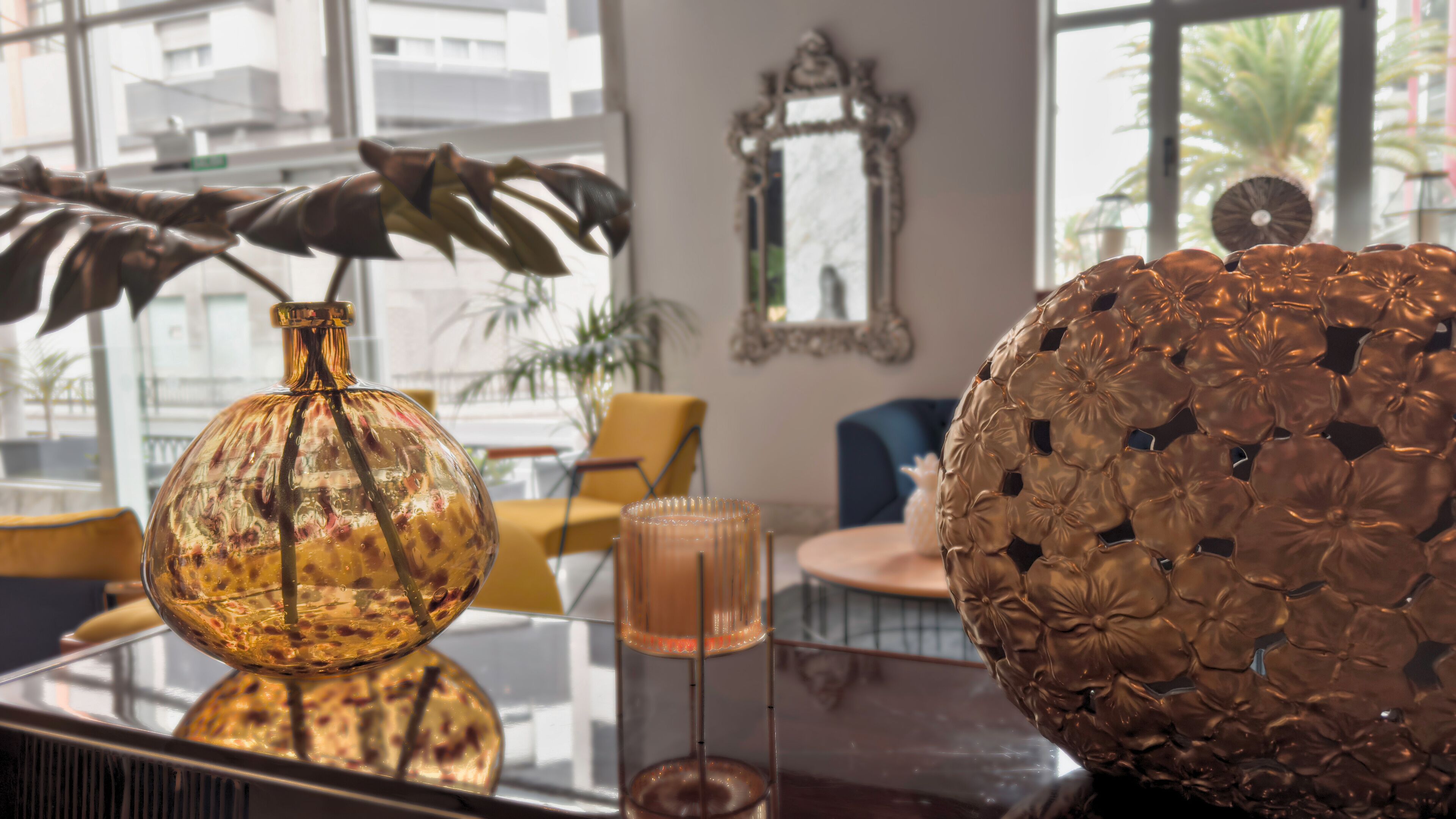 Une pièce avec une table en verre sur laquelle sont disposés un vase, une bougie et une sphère décorative.