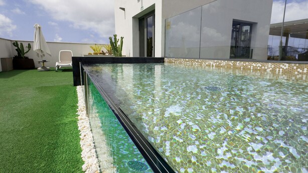 Una piscina con agua cristalina, rodeada de césped artificial verde y plantas en macetas.