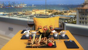 Una mesa con comida, copas de vino y vistas al mar y al puerto.